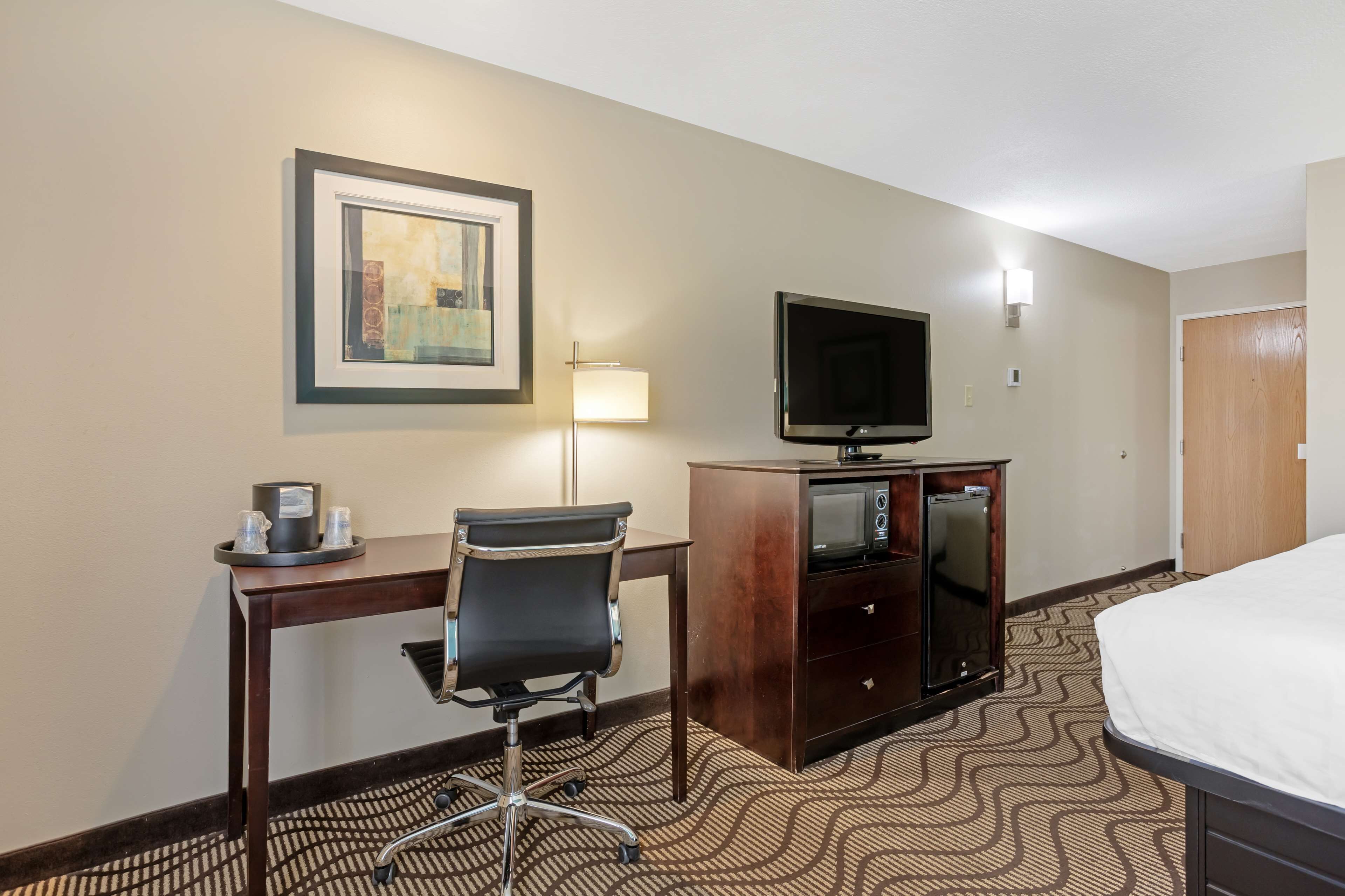 Habitación de hotel con cama, escritorio con silla, televisor, microondas y un cuadro en la pared.