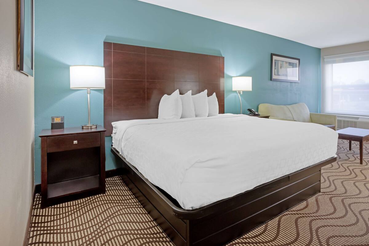 A hotel room with a large bed, two bedside lamps, a nightstand, a chair, and a window with a view.