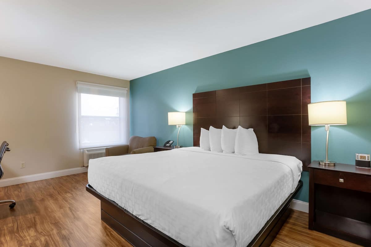 A hotel room with a large bed, two bedside lamps, a nightstand, a chair, and a desk with a lamp.
