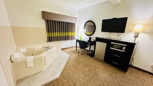 Et badeværelse på et hotel med badekar, et skrivebord, et fjernsyn og et spejl.