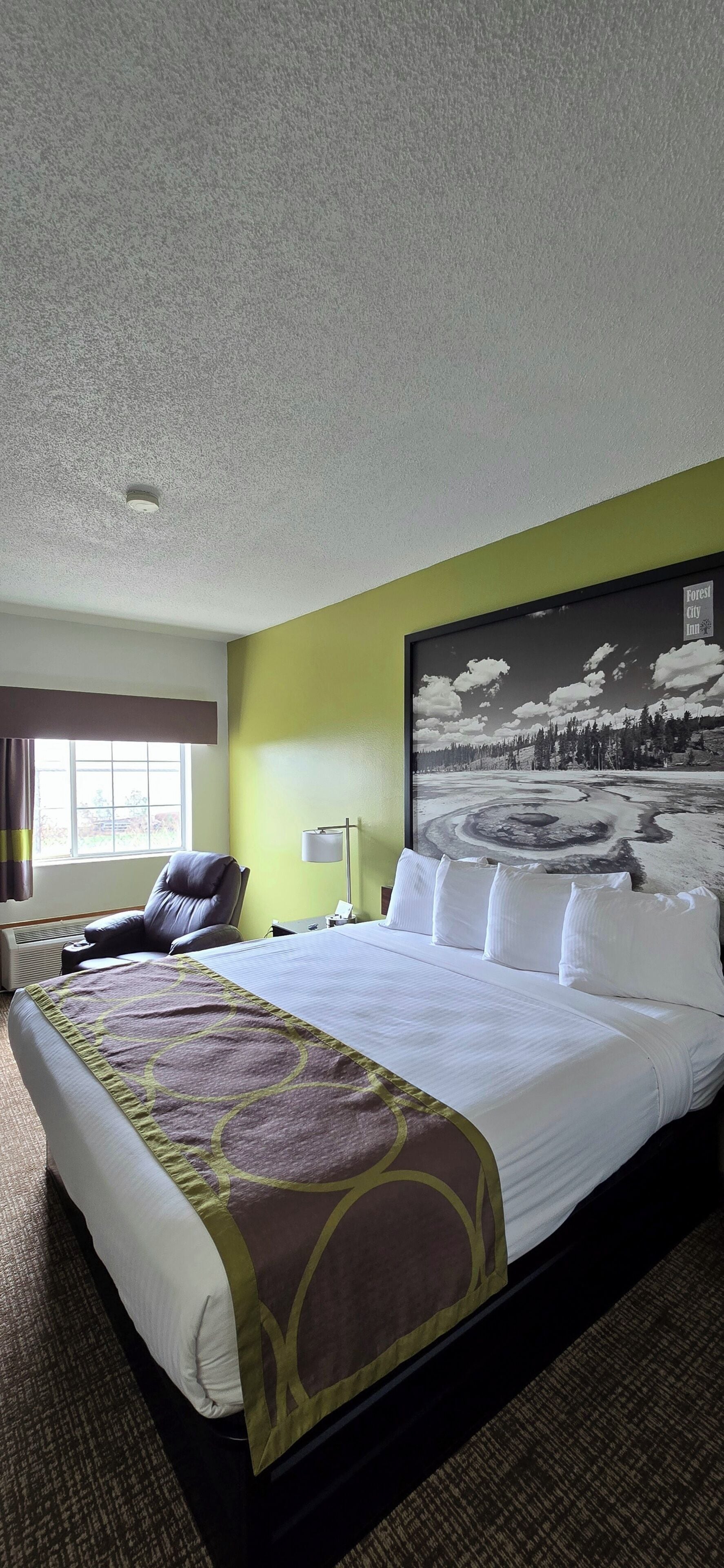 A hotel room with a large bed, a chair, a window, and a painting on the wall.