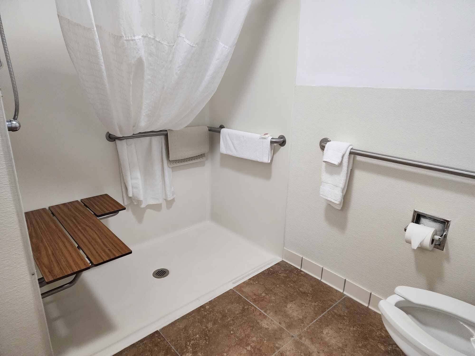 A bathroom with a shower, toilet, and a small wooden shelf.