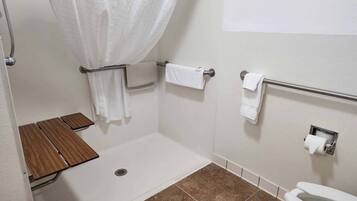 A bathroom with a shower, toilet, and a small wooden shelf.