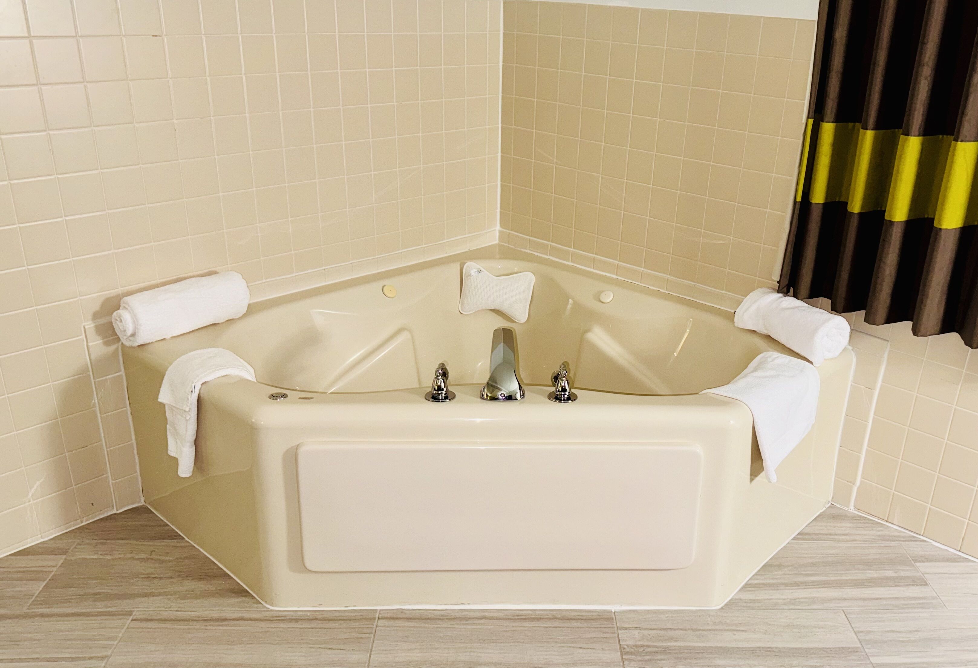 A corner bathtub with two faucets, a built-in seat, and two towels.