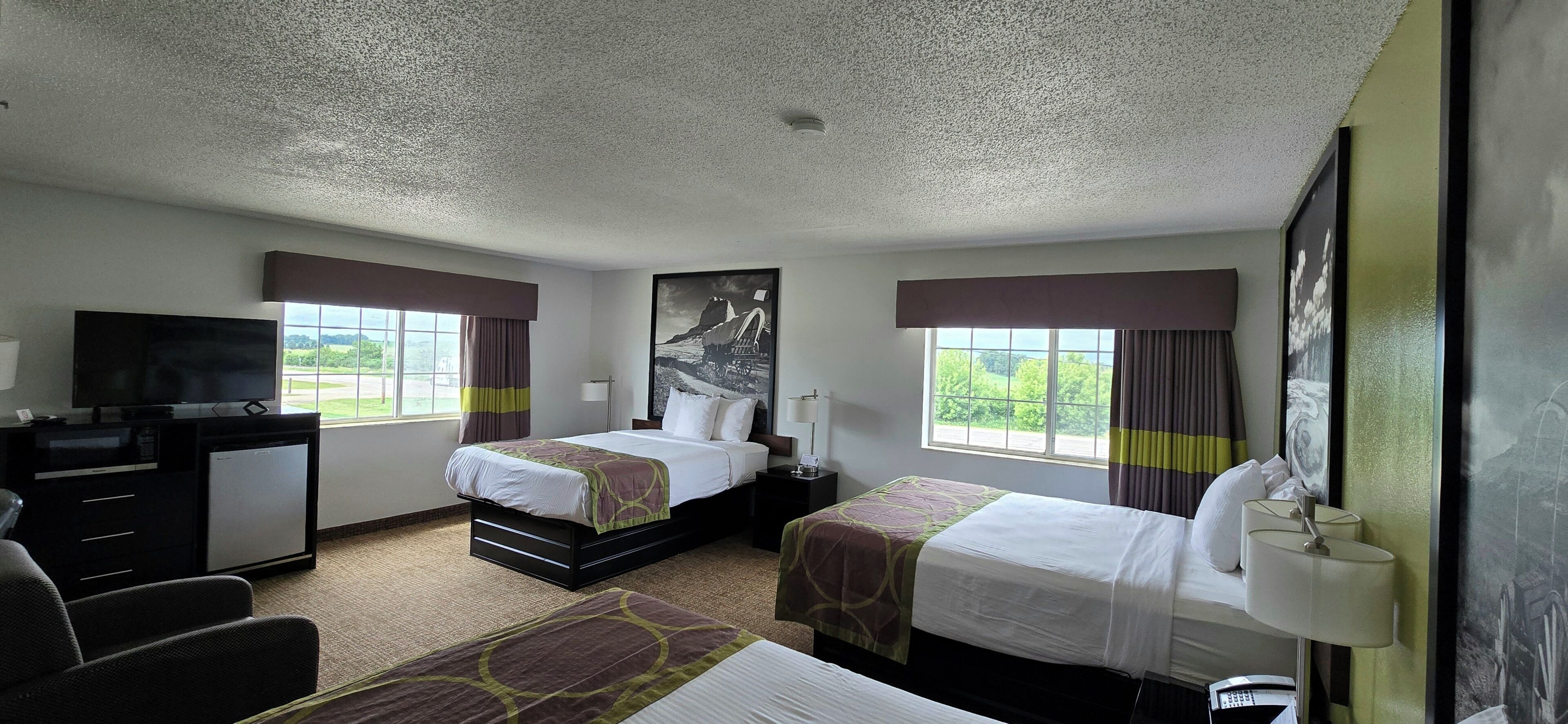 A hotel room with two beds, a desk, a television, and a view of the outdoors.