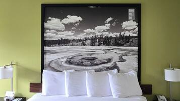 A hotel room with a bed, a nightstand, a lamp, and a wall with a nature-themed artwork.