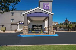 Edificio de Sleep Inn & Suites by Choice Hotels con una entrada moderna, pilares de piedra y una bordilla azul.
