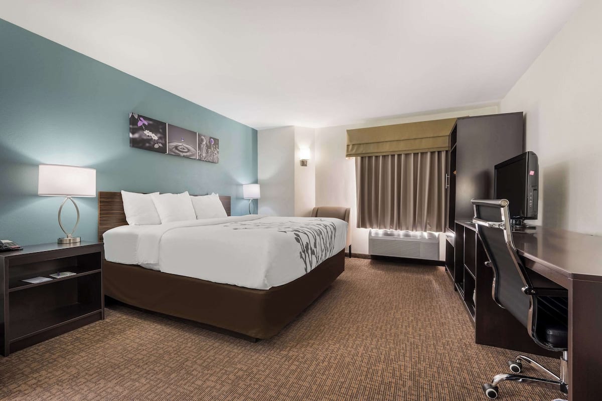 A hotel room with a large bed, a desk with a computer, a TV, and a window with curtains.