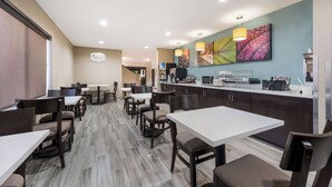 A hotel dining area with multiple tables and chairs, a kitchen counter, and a wall with colorful artwork. - Sleep Inn & Suites Cullman I-65 exit 310 (Cullman)
