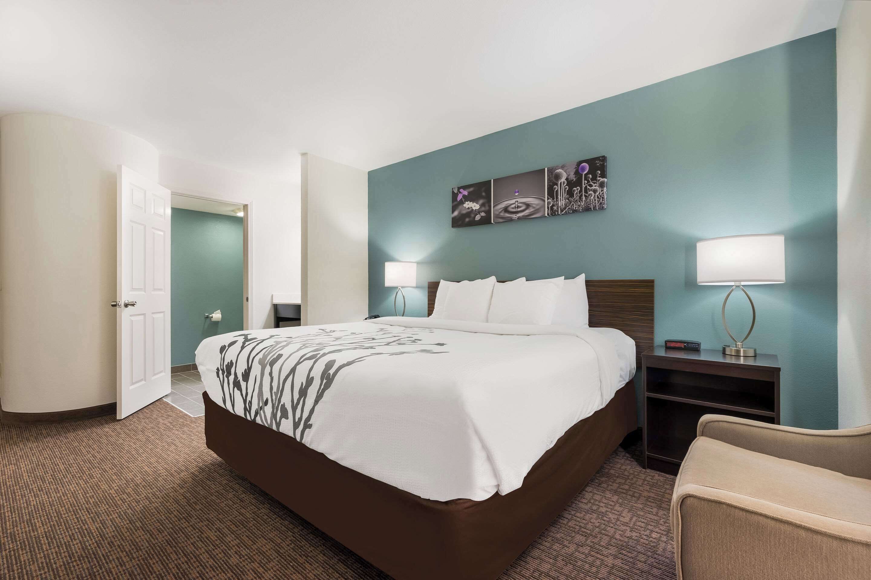 A hotel room with a large bed, two bedside tables with lamps, a chair, and a wall with artwork.