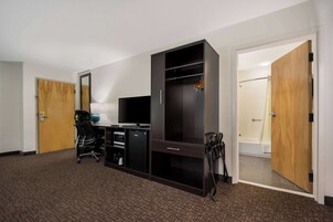 Habitación de hotel con escritorio, silla, armario y zona de ducha.