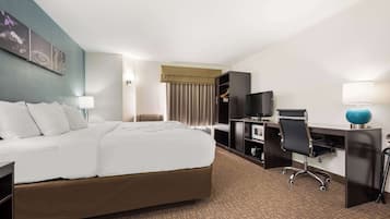 Habitación de hotel con una cama grande, un escritorio con computadora, un televisor y una silla.