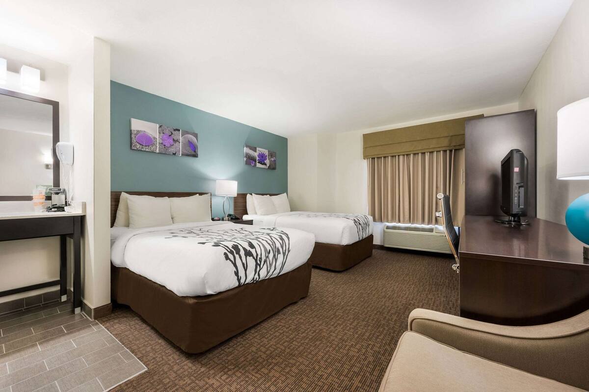 A hotel room with two beds, a desk, a TV, and a bathroom.