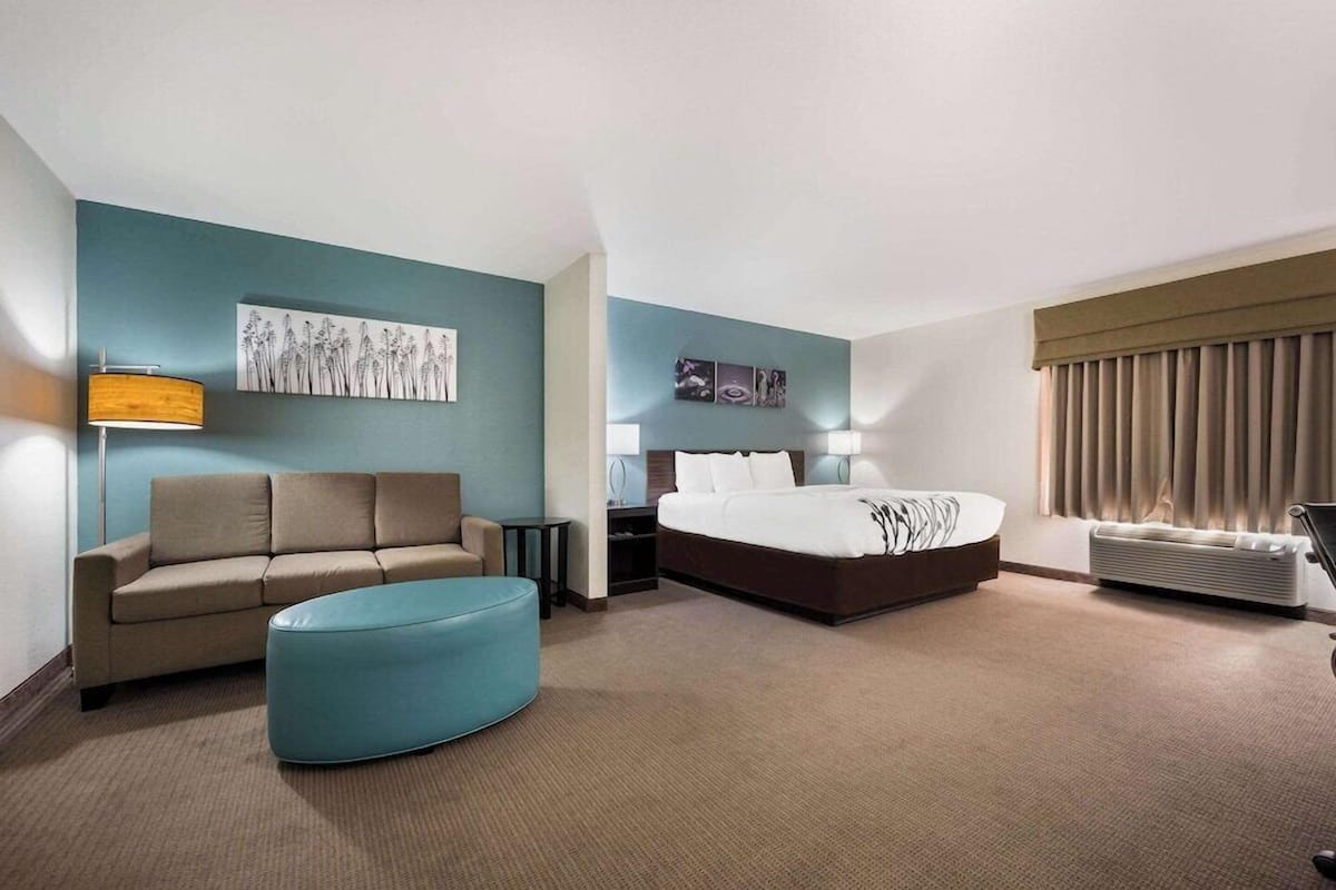 A hotel room with a bed, a sofa, a coffee table, a desk, and a lamp.