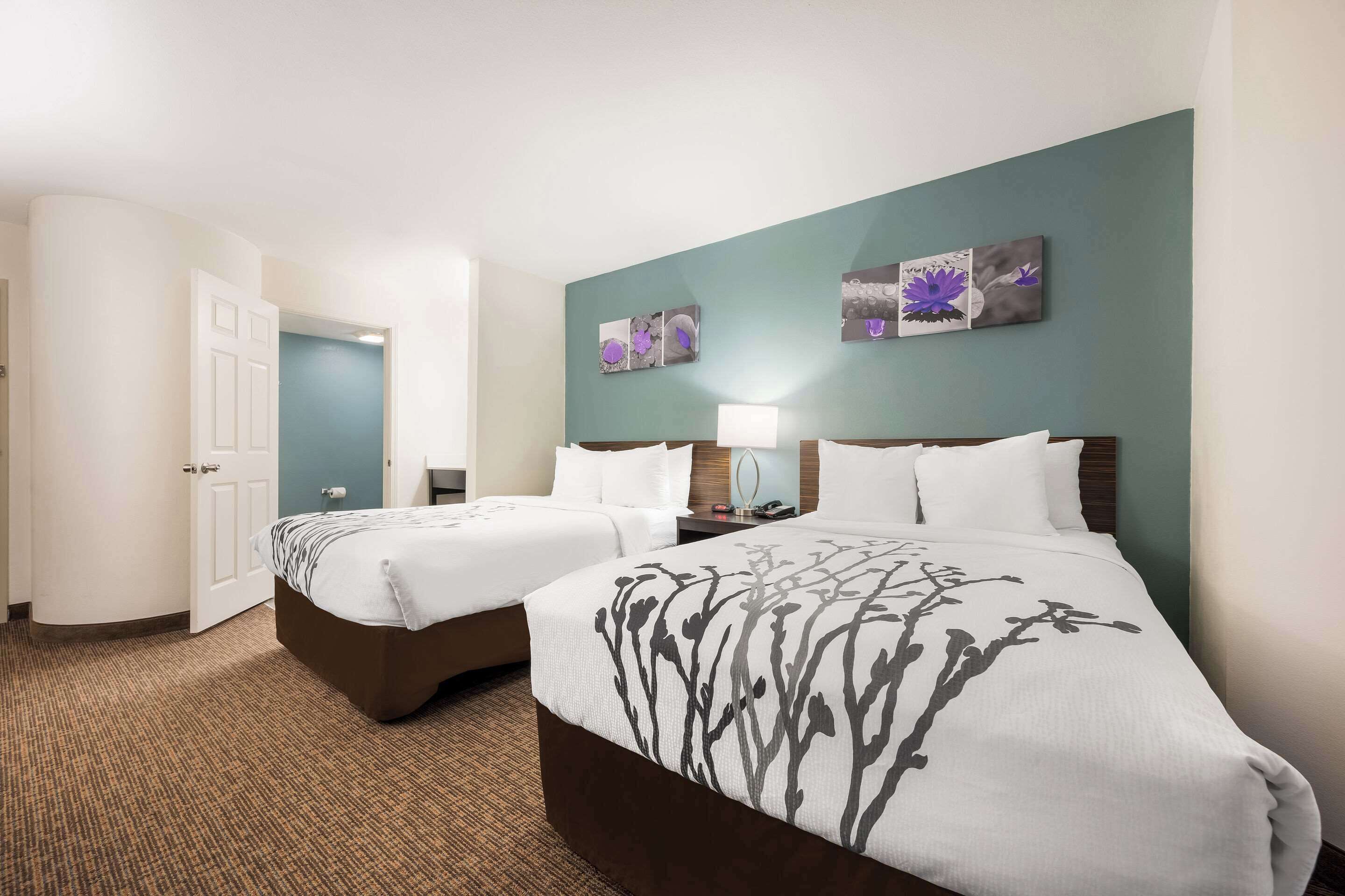 Habitació d'hotel amb dos llits, una tauleta de nit amb una làmpada i obra d'art a la paret.