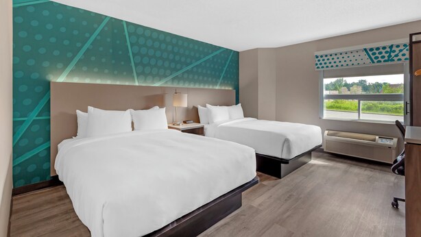Habitación de hotel con dos camas, un ventanal con vistas, un calentador en la pared y un escritorio con silla.