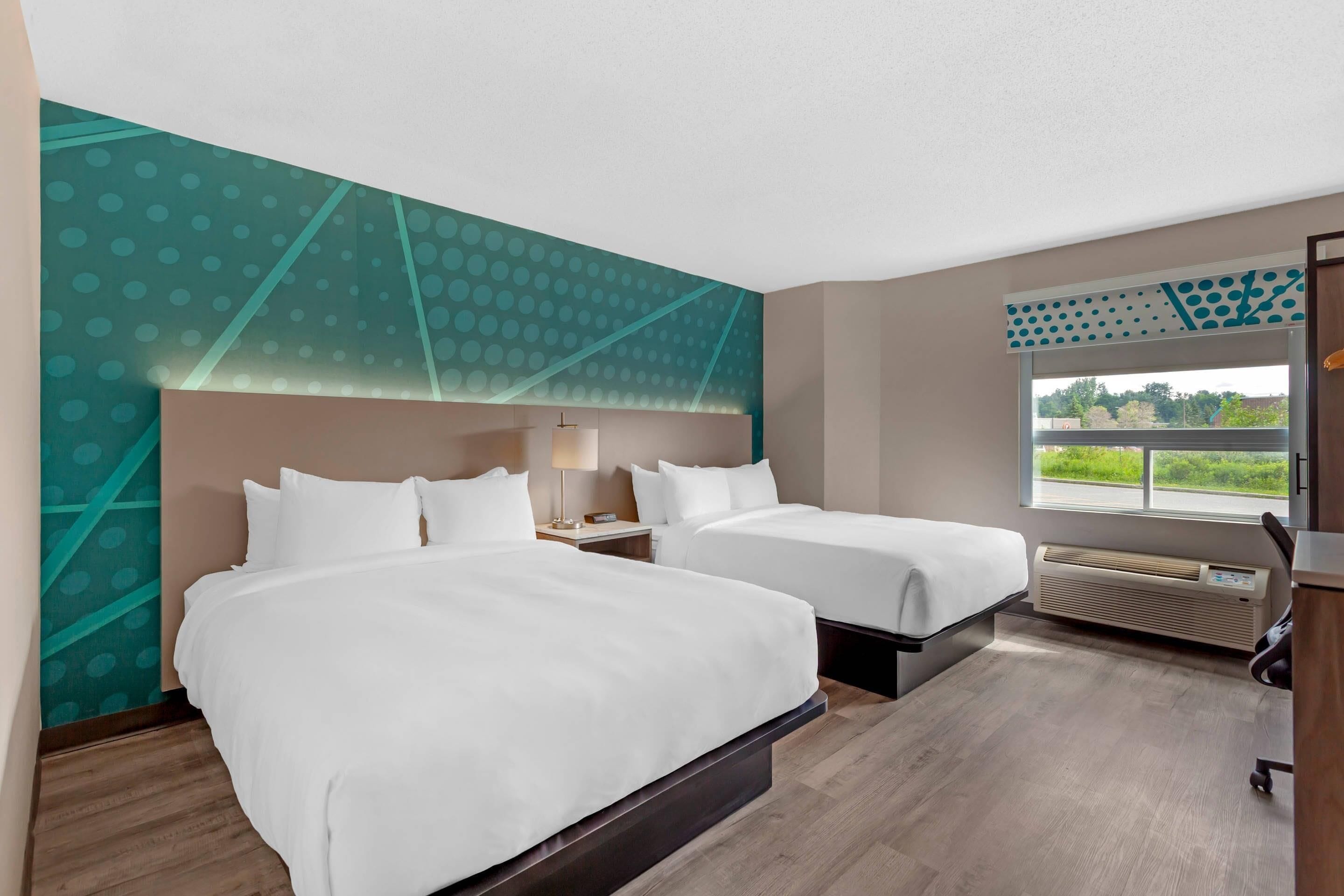 Habitación de hotel con dos camas, un ventanal grande, aire acondicionado de pared y un escritorio con silla.