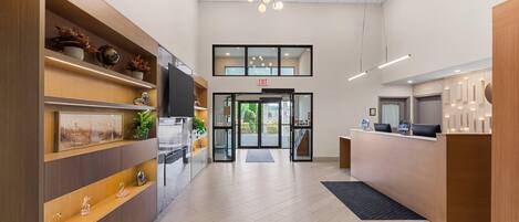 A modern reception area with a wooden reception desk, a flat-screen TV, and a glass door entrance.