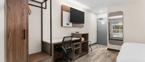 Habitación de hotel con un escritorio de madera, una silla, un televisor de pantalla plana, una cama y un espejo grande.