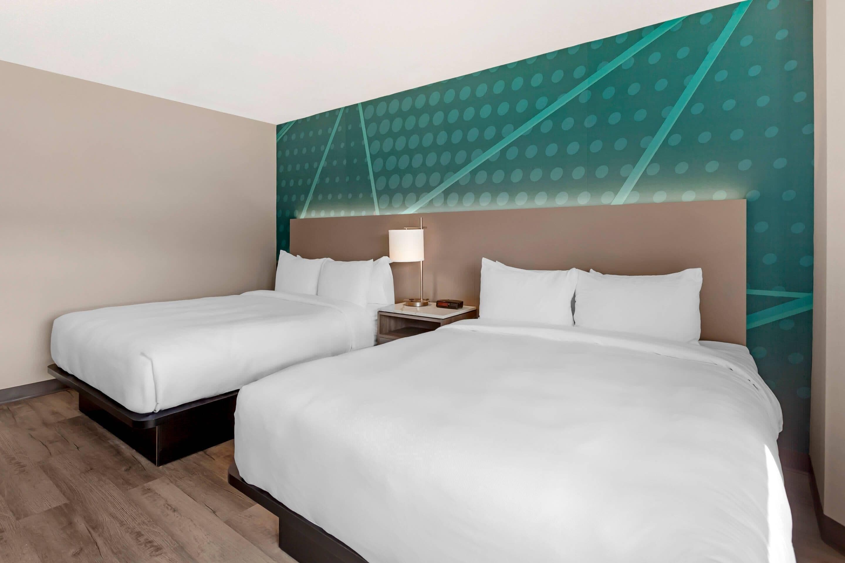 Een hotelkamer met twee bedden, een nachtkastje met een lamp, en een muur met een geometrisch patroon.