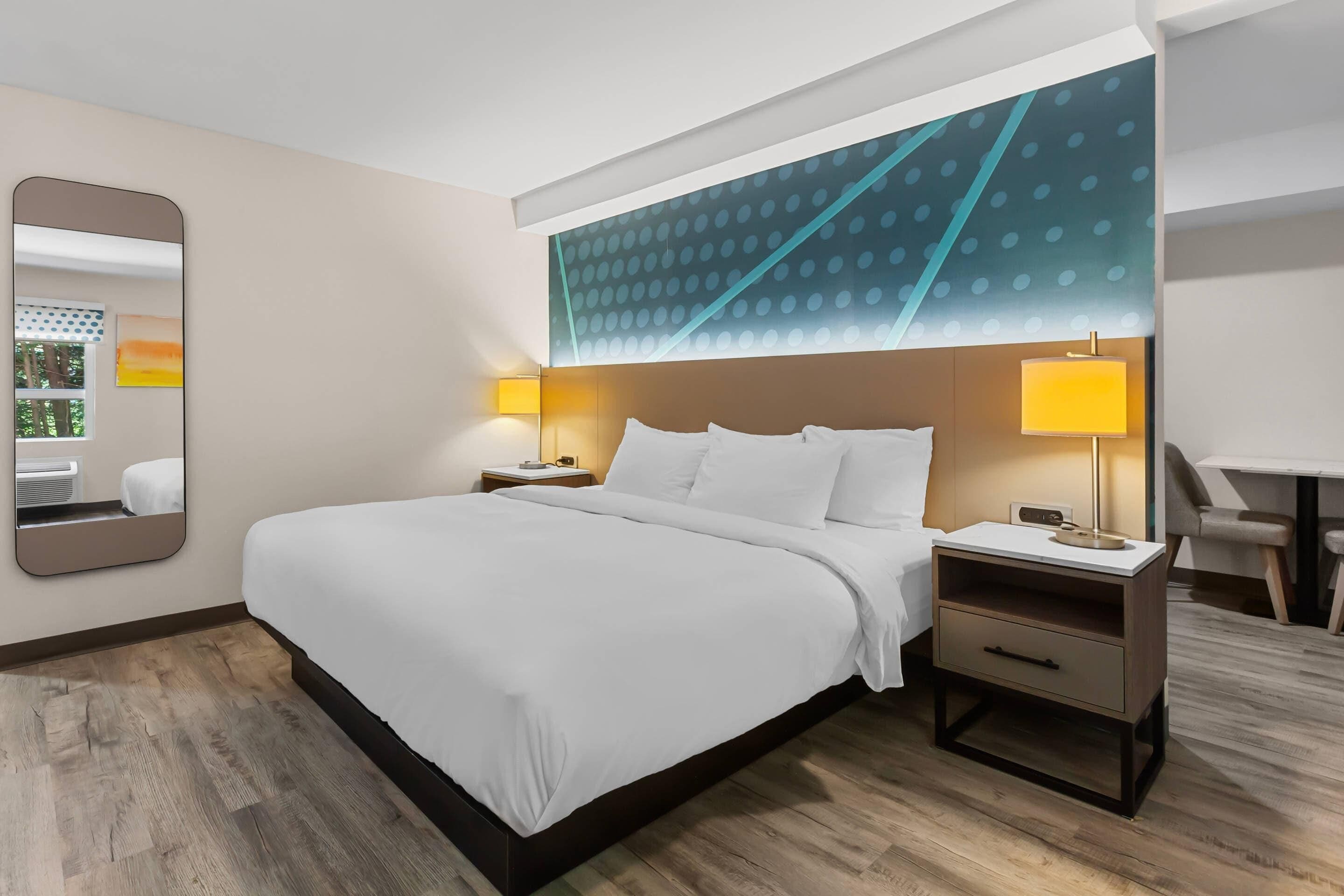 A hotel room with a large bed, two bedside tables with lamps, a mirror, and a wall with a geometric pattern.