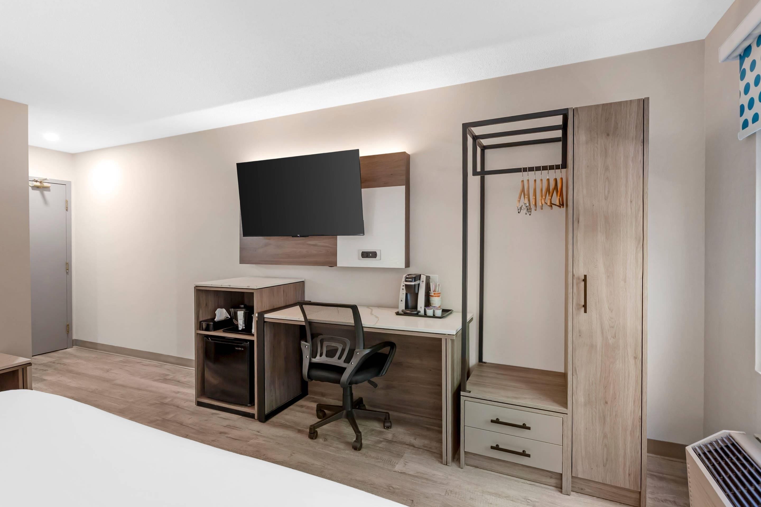 A bedroom with a bed, a desk with a chair, a wardrobe, and a TV mounted on the wall.