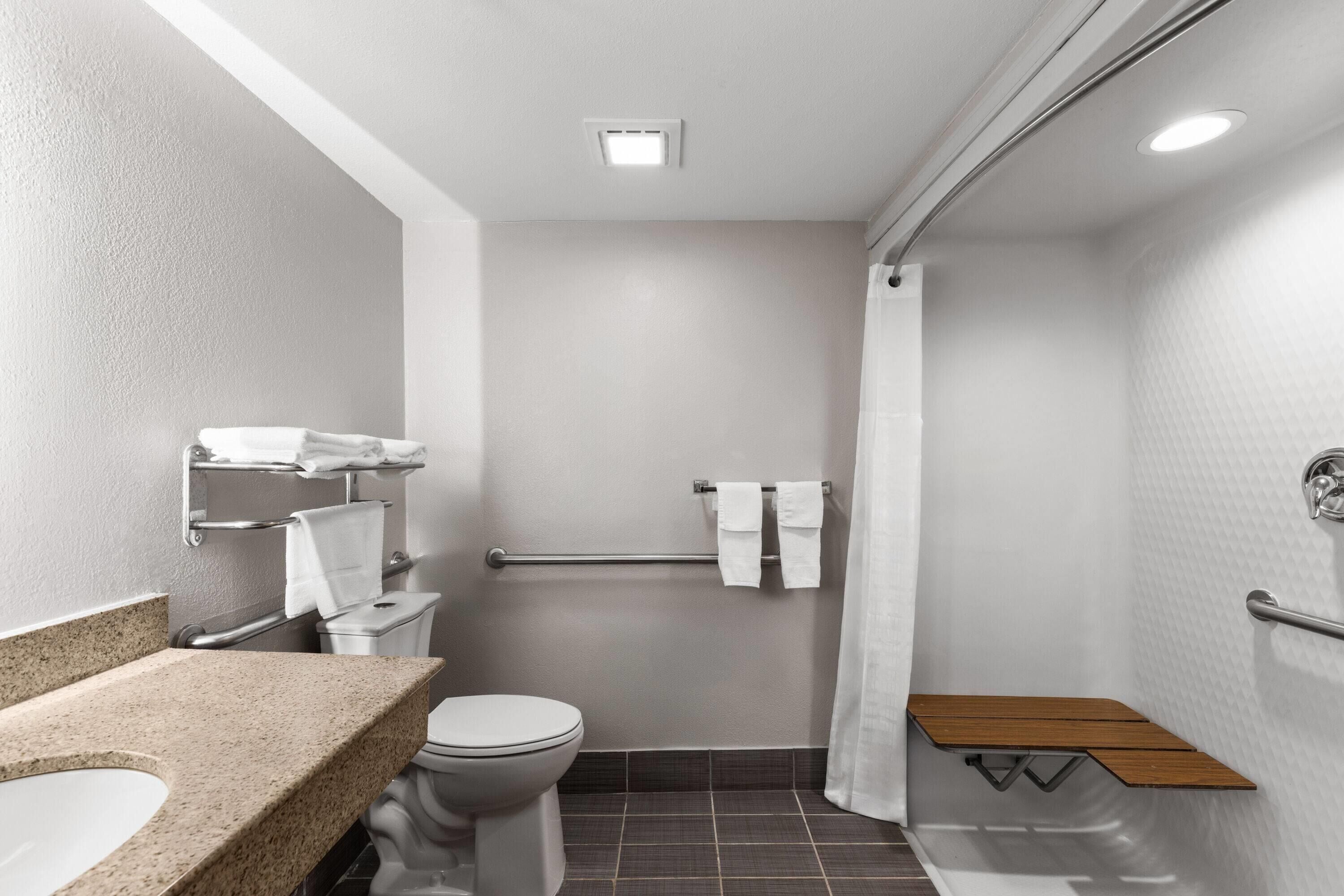 A bathroom with a toilet, sink, shower, and a wooden bench.