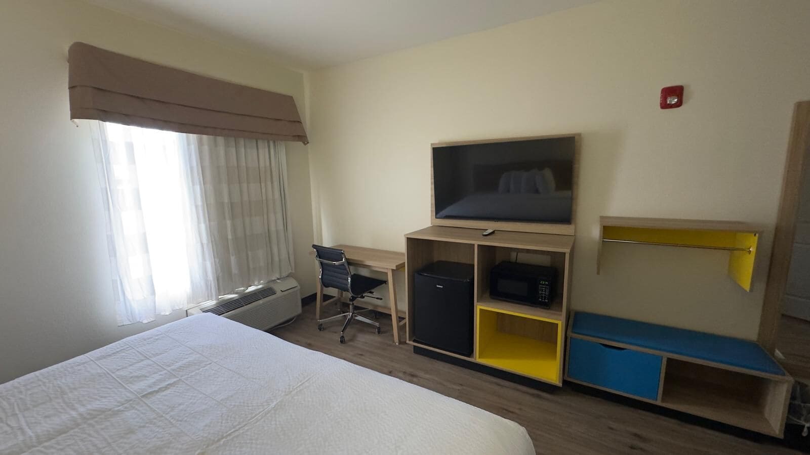 Hotelkamer met een bed, een bureau met stoel, een televisie, een magnetron en een kleine koelkast.