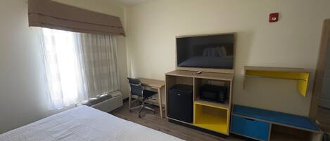A hotel room with a bed, a desk with a chair, a television, a microwave, and a small refrigerator.