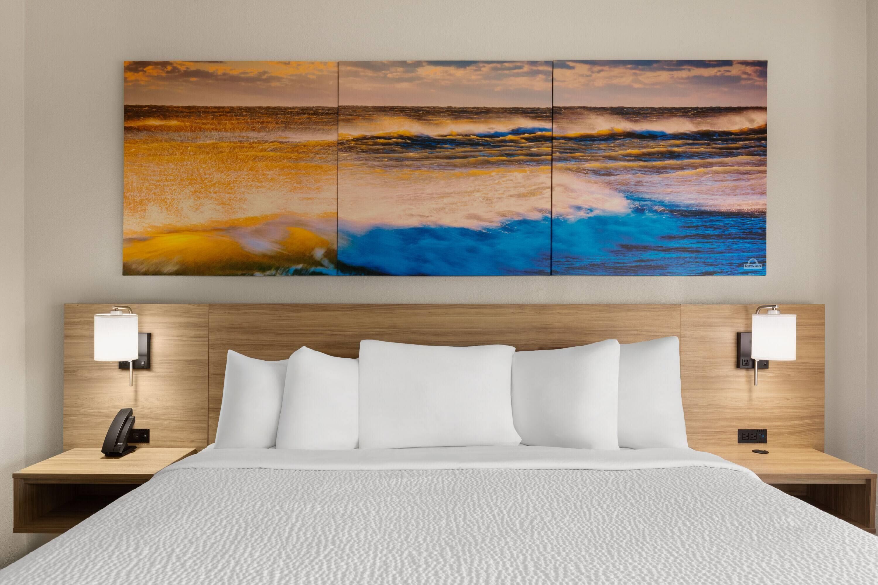 A hotel room with a bed, white bedding, a headboard with a wooden finish, two bedside lamps, and a wall-mounted phone.
