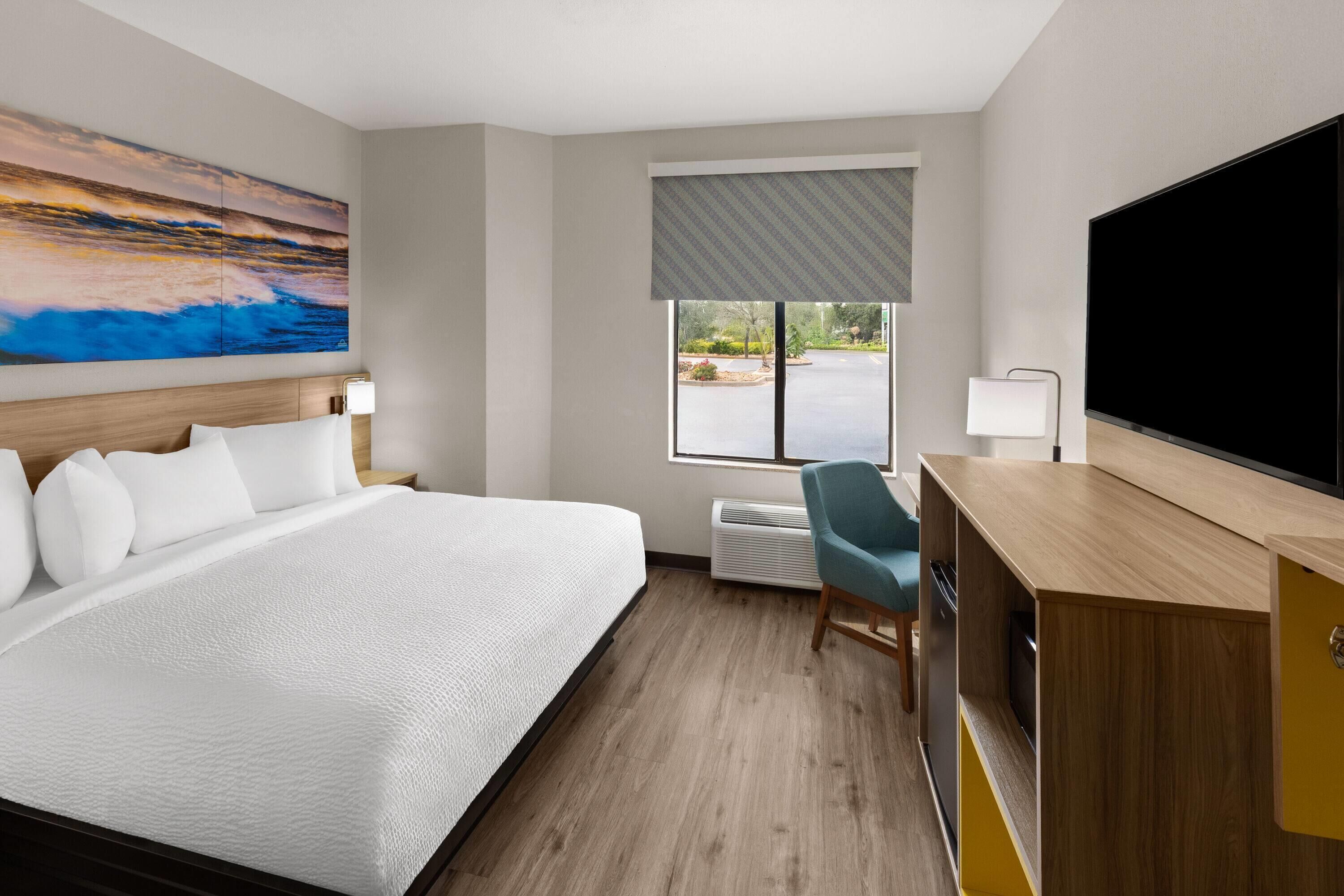 Une chambre d’hôtel équipée d’un lit, d’un bureau, d’une chaise, d’une télévision et d’une fenêtre donnant sur l’extérieur.