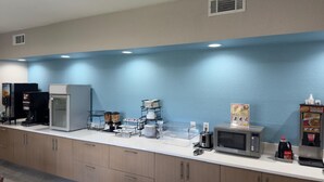 Un área de desayuno autoservicio con máquinas de café, un microondas y dispensador de bebidas.