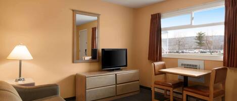 A hotel room with a sofa, a TV on a dresser, a small table with chairs, and a window with curtains.