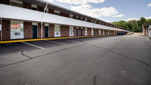 A motel with a row of rooms, a parking lot, and a building in the background. - Econo Lodge Inn & Suites Northborough - Westborough (Northborough)