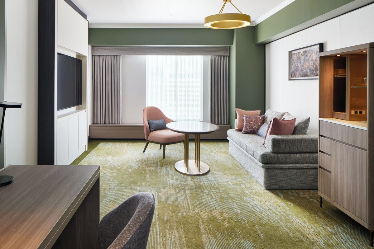 A modern hotel room with a round table, a sofa, a TV, and a cabinet.