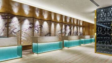 A modern hotel lobby with marble wall panels, teal accent lighting, and a patterned glass partition.