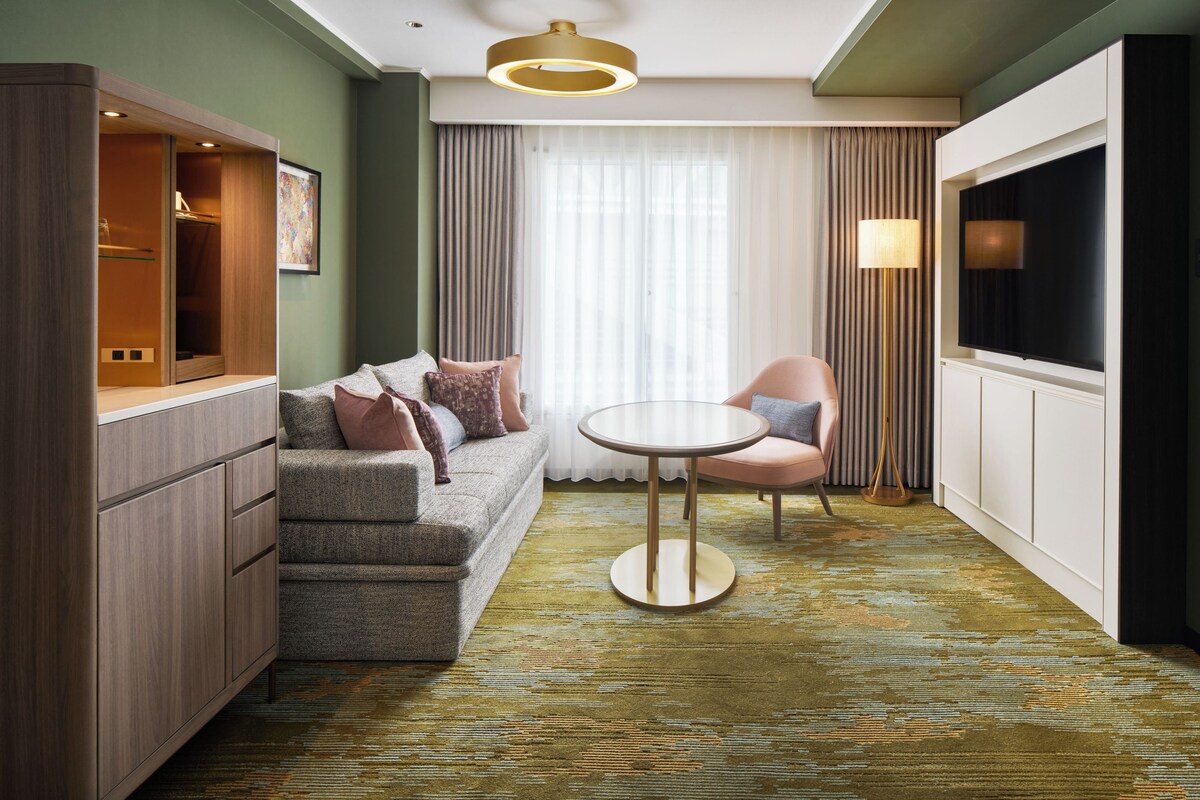 A modern hotel room with a grey sofa, a round table, and a TV.