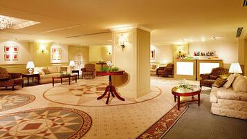 A spacious lobby with a central round table, multiple seating areas, and a bar with a wine display.