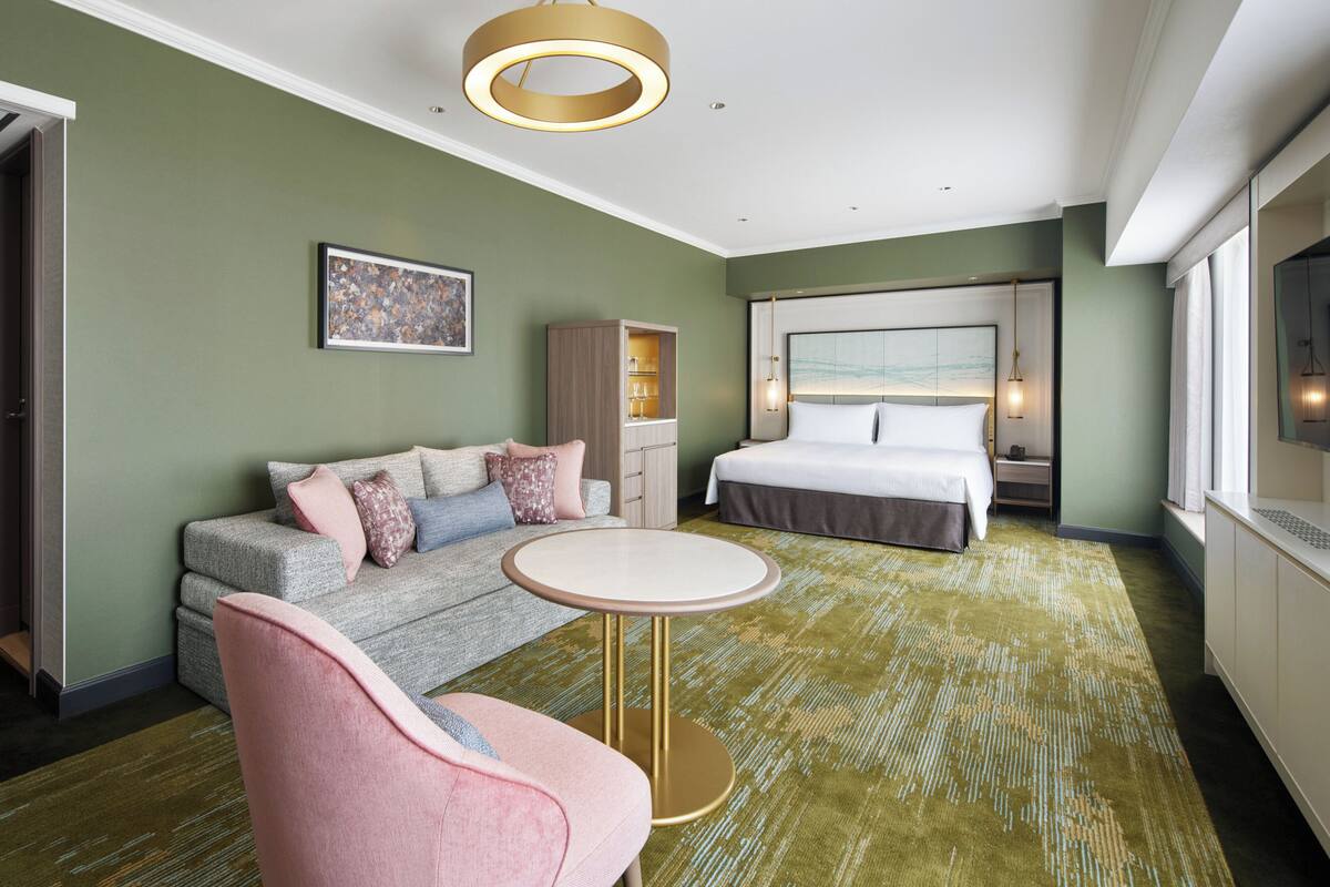 Une chambre d’hôtel avec un lit, un canapé, une petite table ronde et un téléviseur.