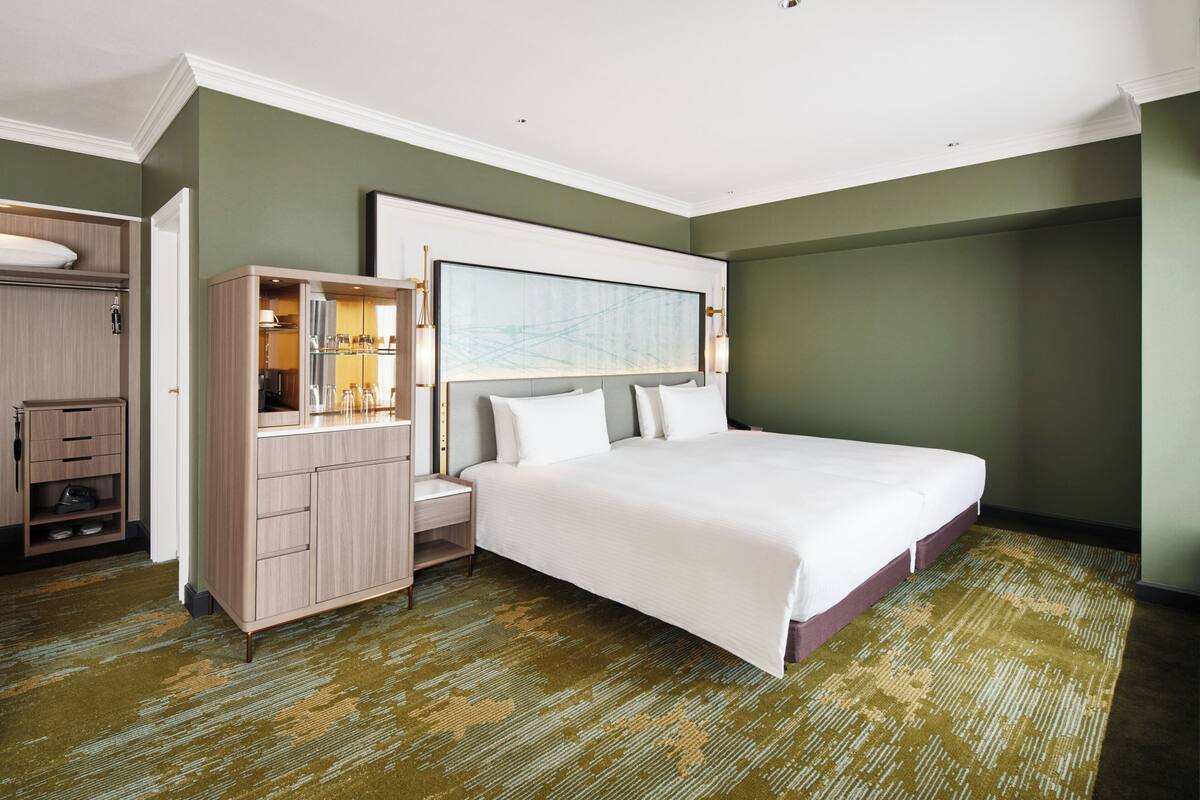 Une chambre d’hôtel avec un grand lit, une armoire, une coiffeuse avec un miroir et un grand tableau abstrait accroché au mur.