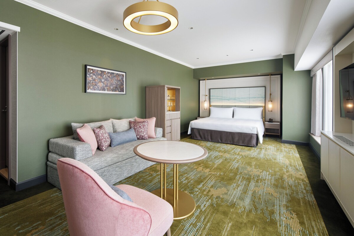 A hotel room with a bed, a sofa, a small round table, and a television.