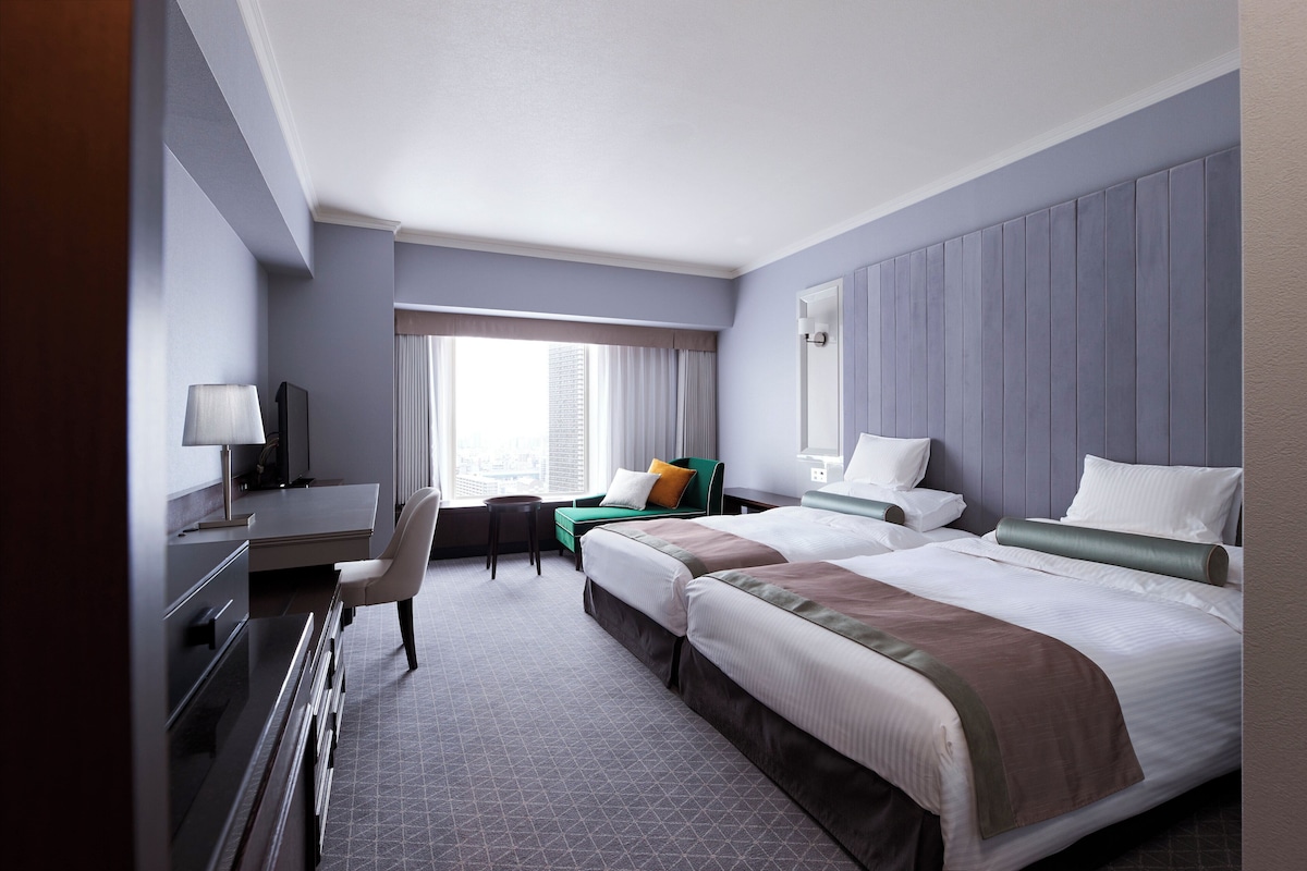 A hotel room with two beds, a desk, a chair, and a window with curtains.