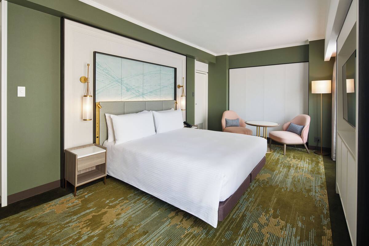 Une chambre d’hôtel avec un grand lit, une table de chevet, une chaise, une petite table et une lampe fixée au mur.