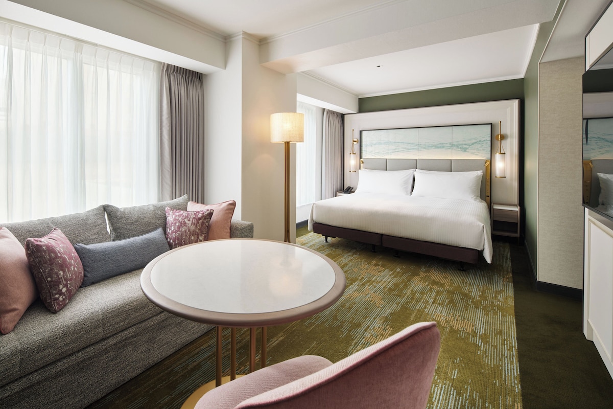 A hotel room with a bed, a sofa, a round table, and a chair.