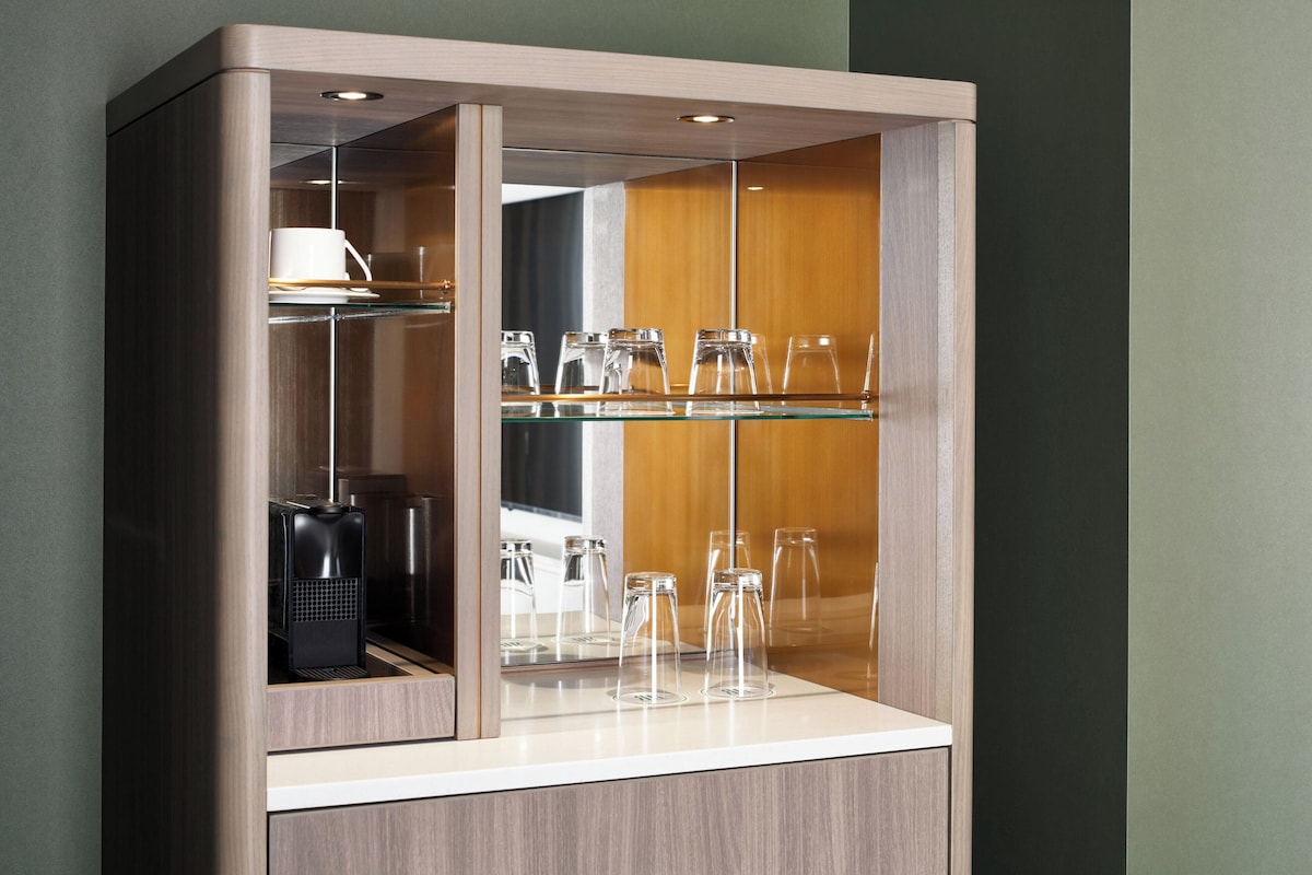 A cabinet with glass shelves displaying clear glassware and a white cup.