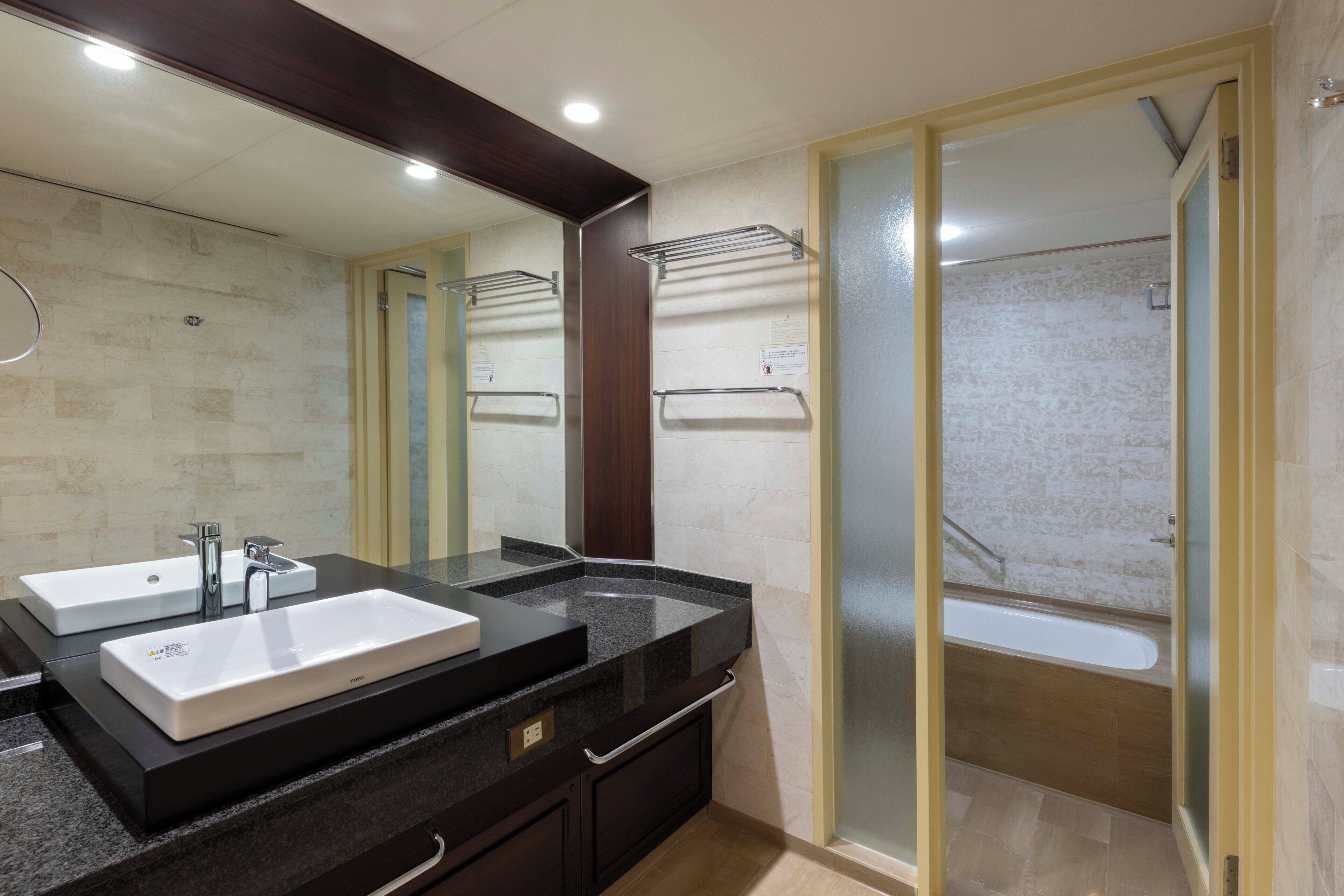 A modern bathroom with two sinks, a large mirror, and a walk-in shower.