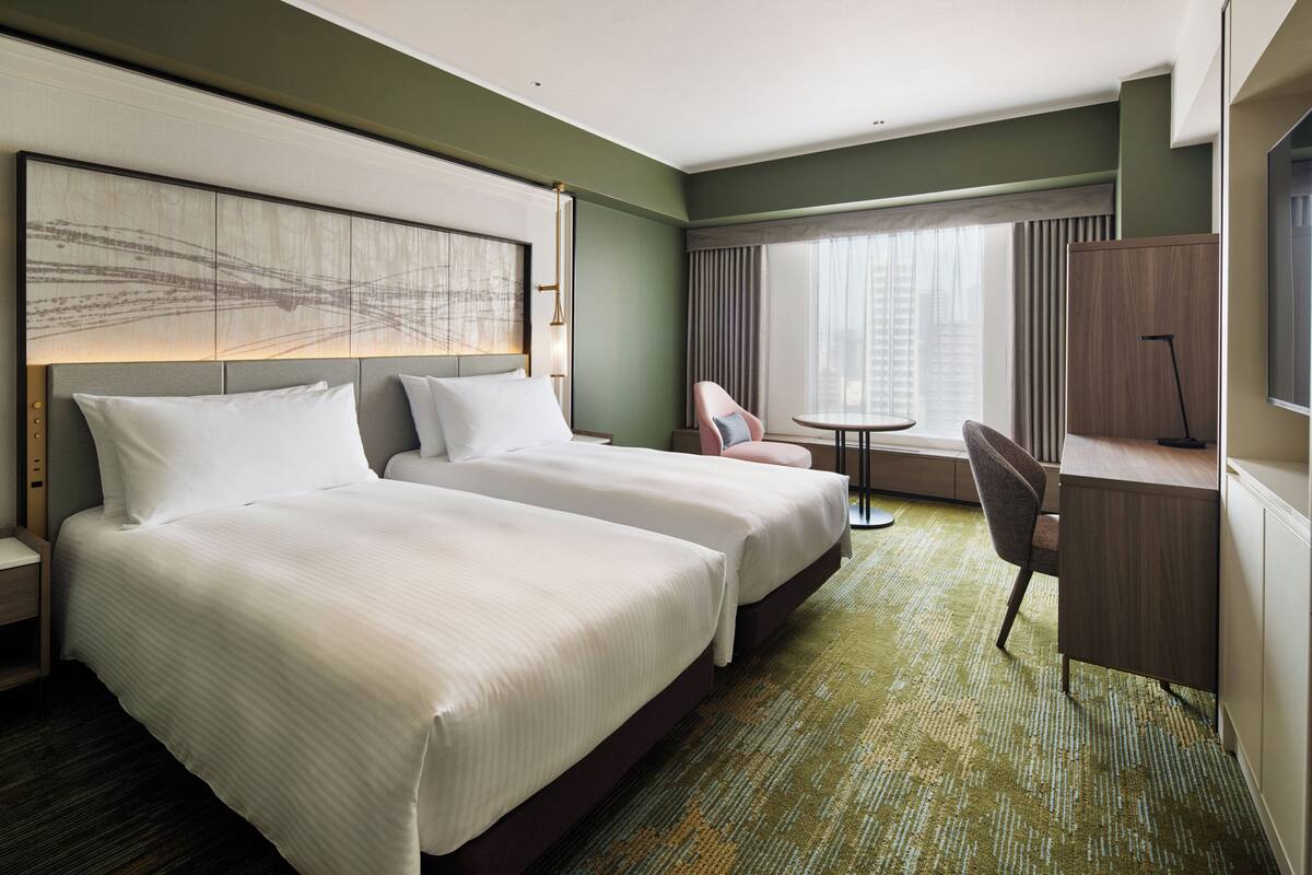 Une chambre d’hôtel avec deux lits, un bureau, une chaise et une vue sur la ville.