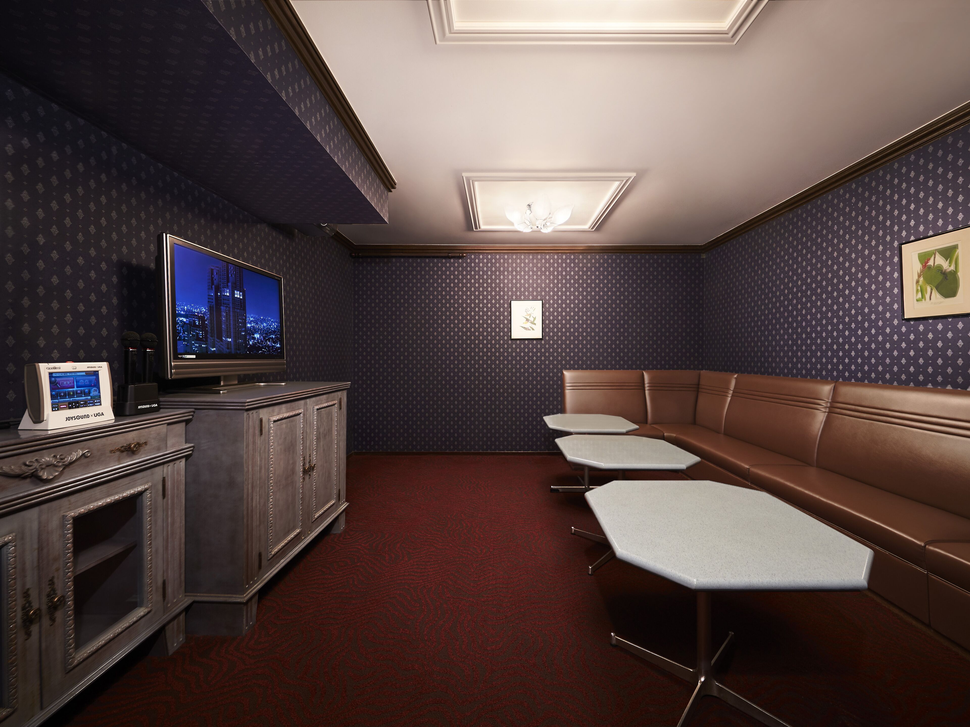 A room with a dark patterned wall, a brown leather couch, a television, and a small table with a microphone.