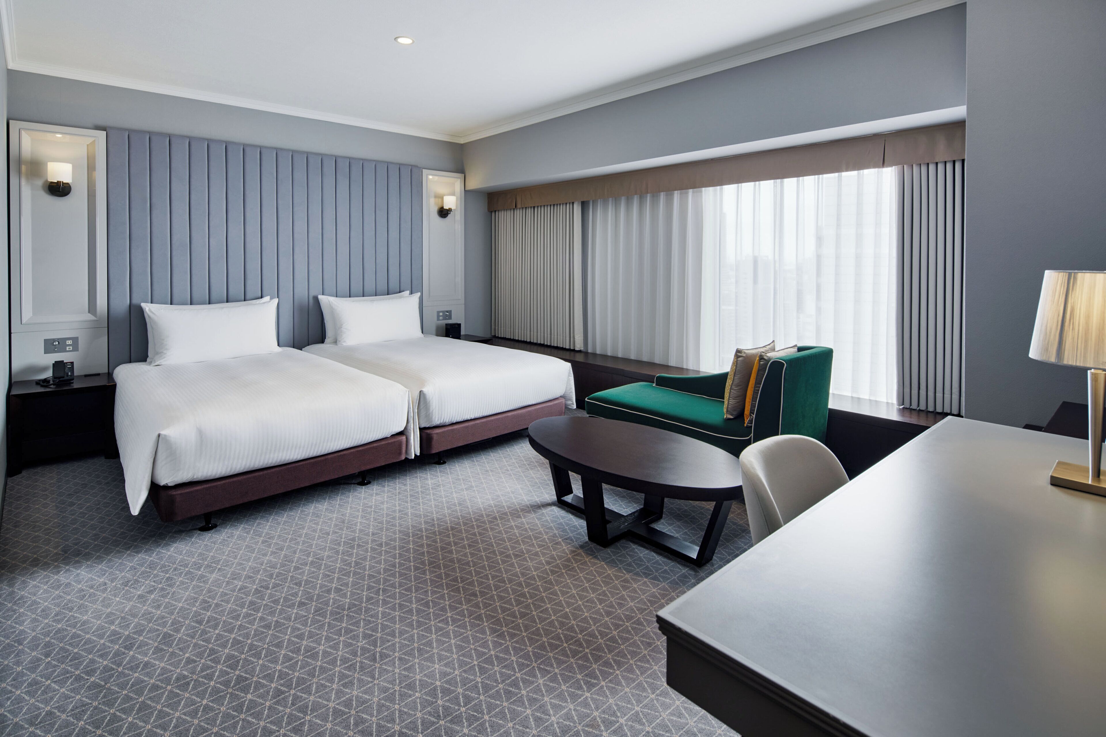 A hotel room with two beds, a desk, a chair, and a window with curtains.