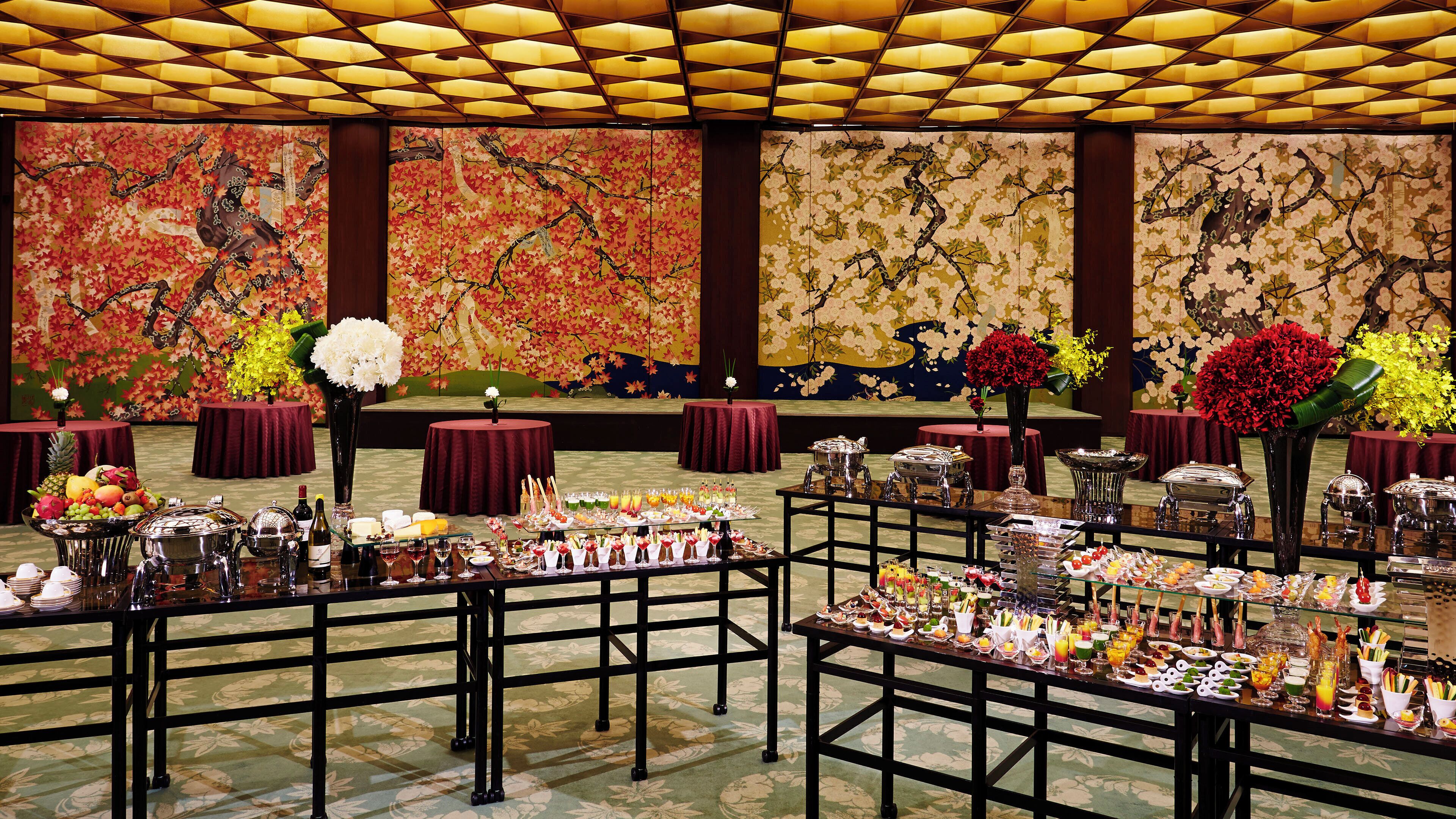 A banquet hall with tables set for a formal event, featuring floral arrangements and a variety of food and drink options.